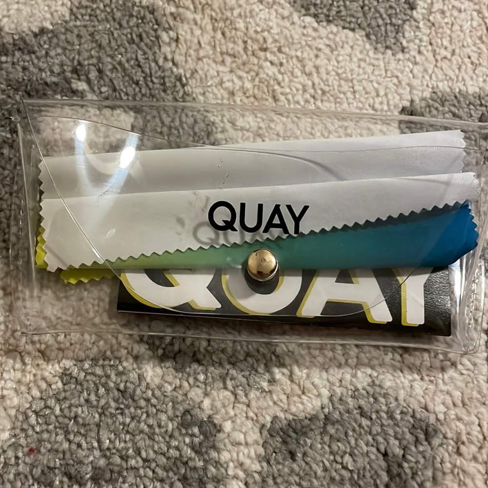 Clear QUAY sunglasses case with blue, green, and yellow cleaner